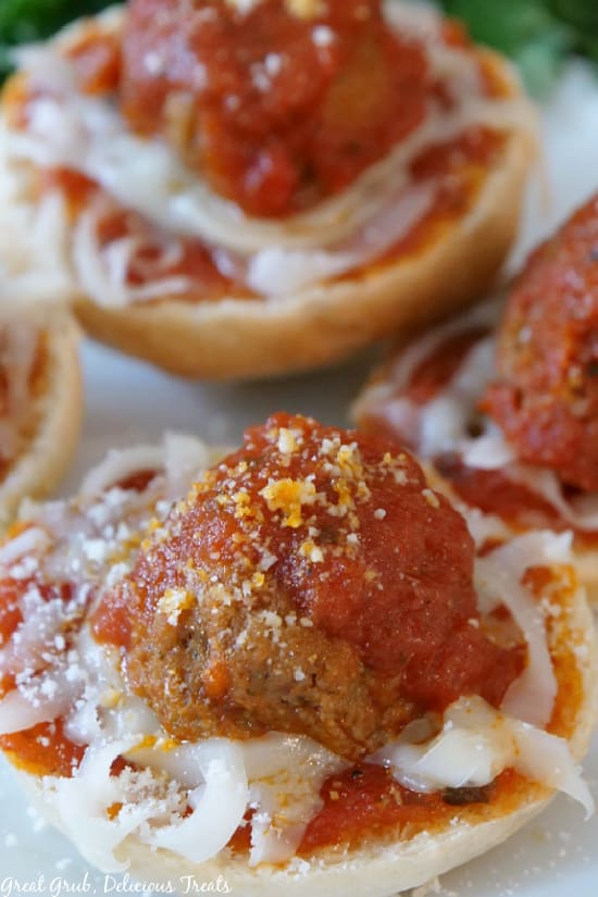 Meatball Bagel Bites are a quick and easy snack that is perfect for any weekday. A close up picture of Meatball Bagel Bites on a white plate, showcasing the melted mozzarella cheese, cooked meatballs, tomato sauce, and parmesan cheese.