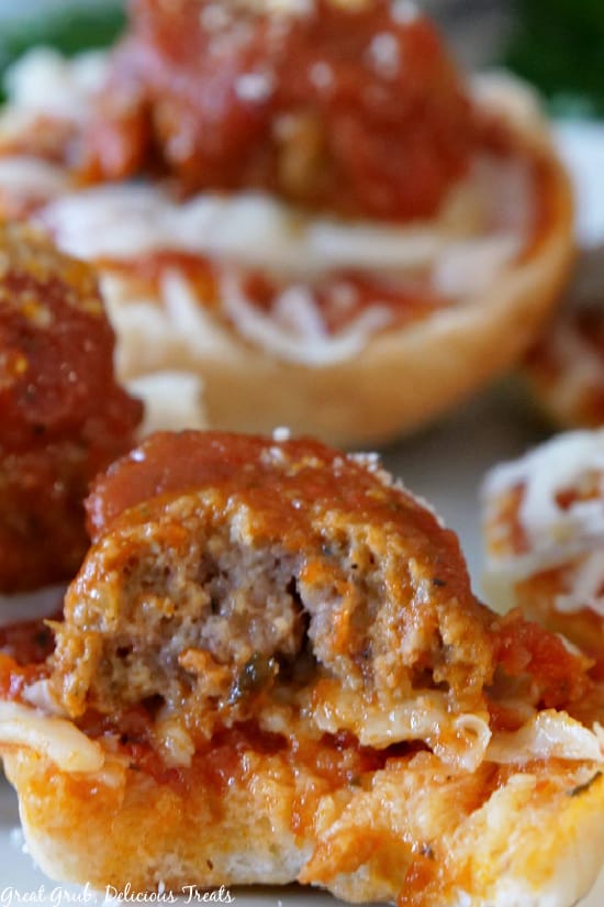 Meatball Bagel Bites are delicious, homemade, bite-sized bagels topped with spaghetti sauce, a deliciously cooked meatball, shredded mozzarella cheese, and parmesan cheese. A close up picture of Meatball Bagel Bites with a bite taken out.