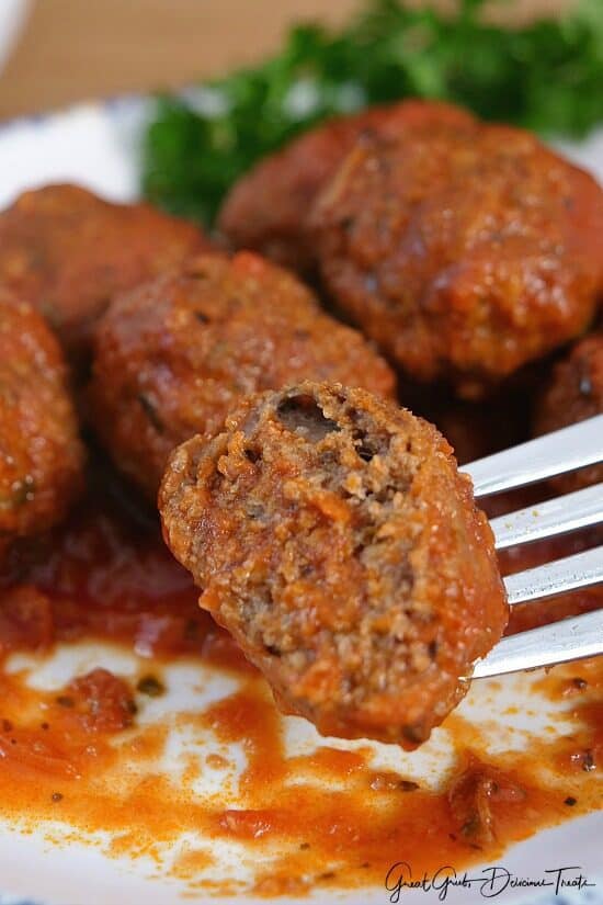 A close up of a meatball on a fork with a bite taken out of it.