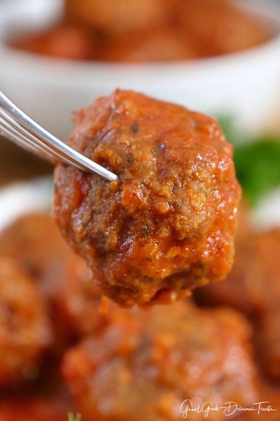 Homemade Italian Meatballs taste delicious, are bite-size and savory, and a scrumptious appetizer recipe. A single meatball on a fork held close to the camera lens.