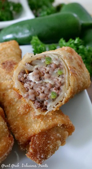 Cheesy Ground Beef Egg Rolls are crispy, crunchy egg rolls filled with deliciously seasoned ground beef, two types of cheese and fried to a golden brown. Three cheesy ground beef egg rolls on a white plate with one with a bite taken out showing the inside meat mixture.