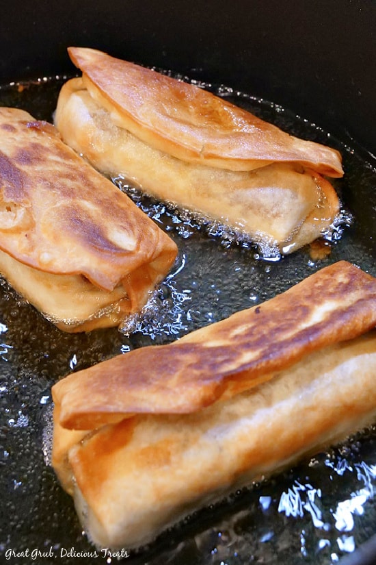 Fried Burritos are a crispy, crunchy and delicious burrito recipe that is full of beef, pork, cheese and more. Three fried burritos being fried in oil.