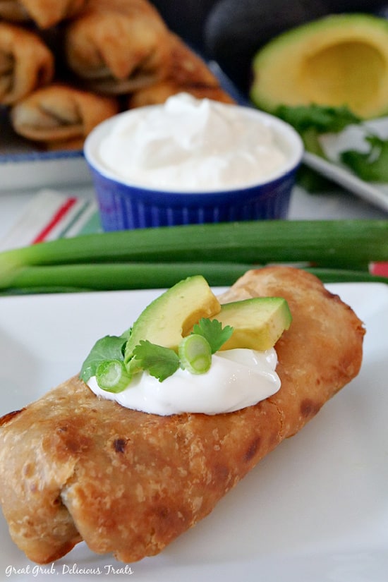 Fried Burritos are a delicious beef, pork, bean burrito loaded with cheese and much more, then fried to a golden brown. A white plate with a fried burrito with sour cream, sliced avocado, green onions and cilantro on top.