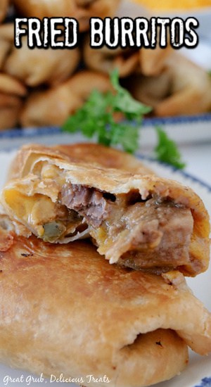 Fried Burritos are loaded with ground beef, pork, beef, refried, pinto and black beans, two types of cheese, green chilies, and fried to perfection. Two fried burritos on a white plate with blue trim, with one burrito with a bite taken out of it.