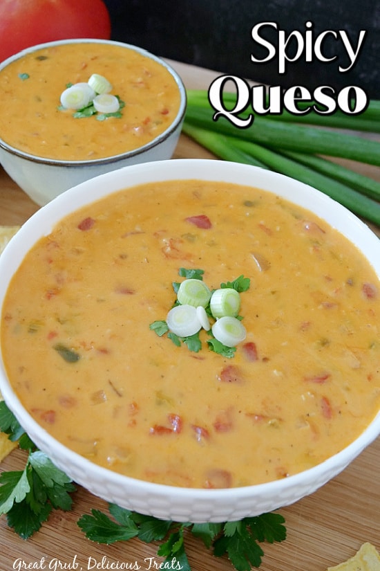 Two white bowls, on a wood cutting board, filled with spicy queso topped with sliced green onions and cilantro.