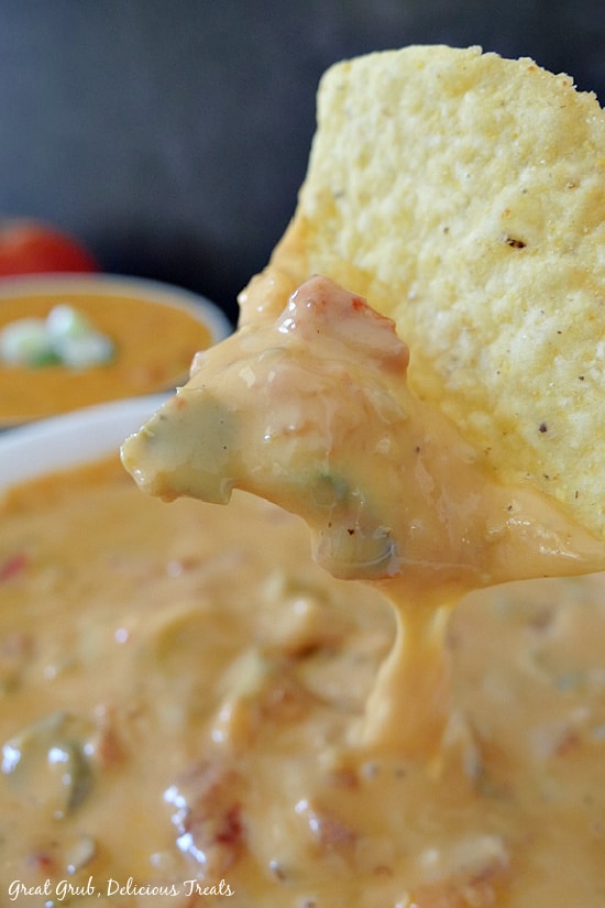 Spicy Queso is not only spicy, it's downright delicious and makes the perfect dip recipe for any party, game day event, or a midday snack. A white bowl filled with spicy queso and a close up shot of a tortilla chip that has been dipped into the queso.