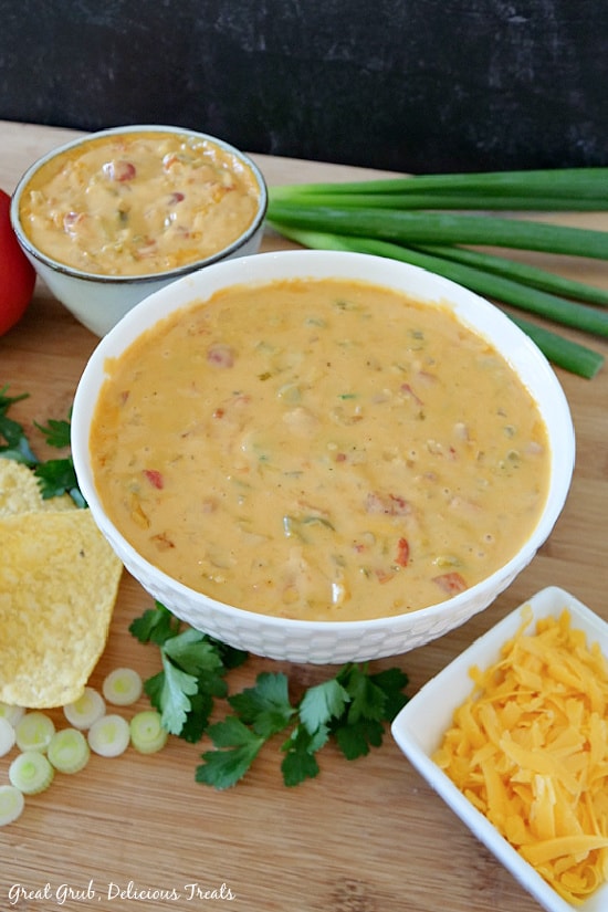 This spicy queso dip is a family favorite queso recipe that is perfect for the next super bowl party, any game day event or just a midday snack. Two white bowls, placed on a wood cutting board, filled with spicy queso.