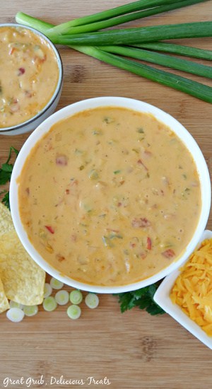 Spicy Queso is the perfect dip appetizer for any game day party, super bowl party, family get-togethers or for a midday snack. A white bowl sitting on a wood cutting board filled with spicy queso.