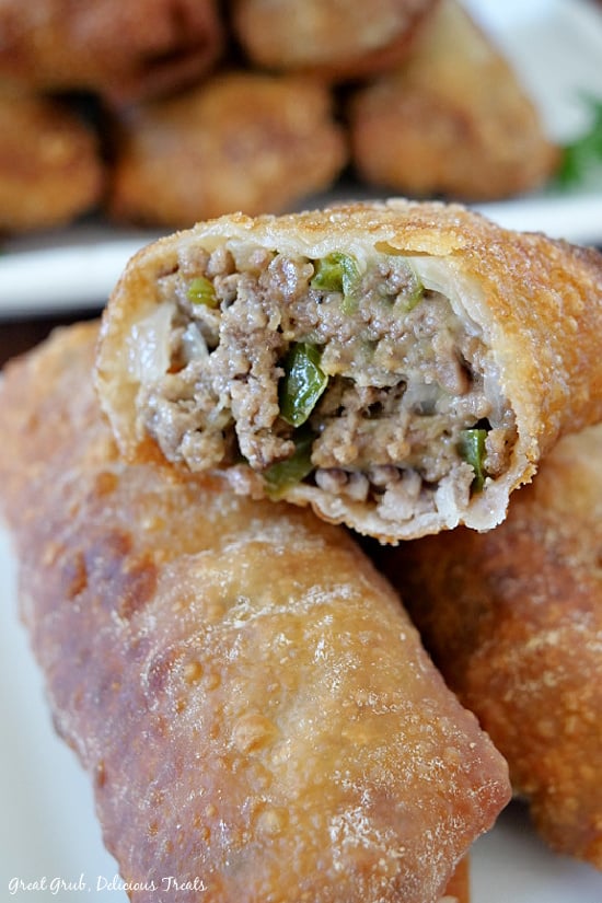 Cheesy Ground Beef Egg Rolls are packed full with deliciously seasoned ground beef, two types of cheese and fried to a golden brown. A cheesy ground beef egg roll, placed on top of two other egg rolls, with a bite taken out of it.