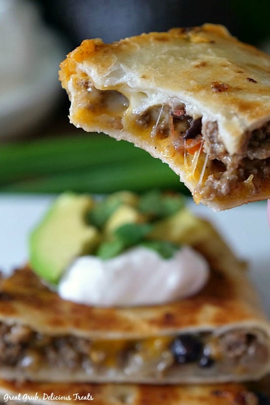 Ground Beef Quesadillas are the perfect, easy quesadilla recipe that is fried crispy and loaded with deliciousness. A piece of quesadilla held above other pieces of quesadilla with a bite taken out of it.