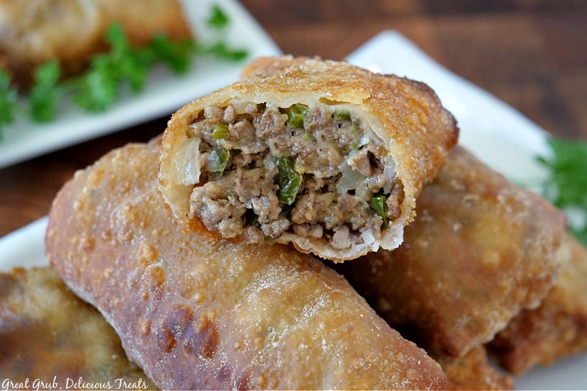 Cheesy Ground Beef Egg Rolls are a delicious and easy egg roll recipe loaded with perfectly seasoned ground beef, two types of cheese and fried to golden brown. A cheesy ground beef egg roll with a bite taken out placed on top of two more egg rolls.