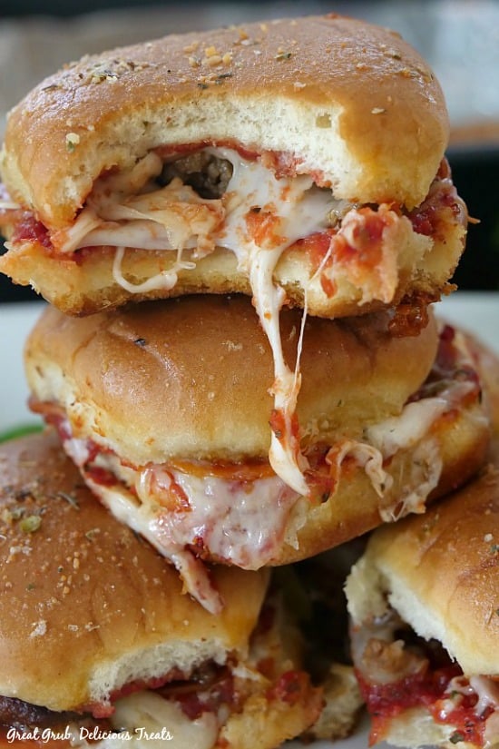 Pepperoni Sausage Pizza Sliders are loaded with cheese, pepperoni and sausage, topped with a buttery topping and then baked until the cheese has melted and is bubbly. Pepperoni Sausage Pizza Sliders stacked on top of each other with a bite taken out and the melted cheese oozing.