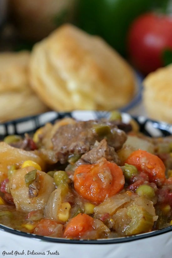 Slow Cooker Beef Stew is a delicious and easy slow cooker beef stew recipe loaded with vegetables. Slow Cooker Beef Stew is in a white and black bowl loaded with beef stew with biscuits in the background.