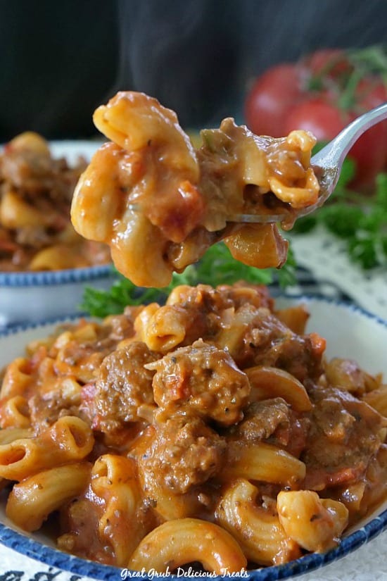 Cheesy Italian Sausage Pasta is a delicious one pot pasta recipe loaded with Italian sausage and cheese. Cheesy Italian Sausage Pasta is a picture of a white bowl with blue trim with a fork full of pasta being held over the bowl of pasta.