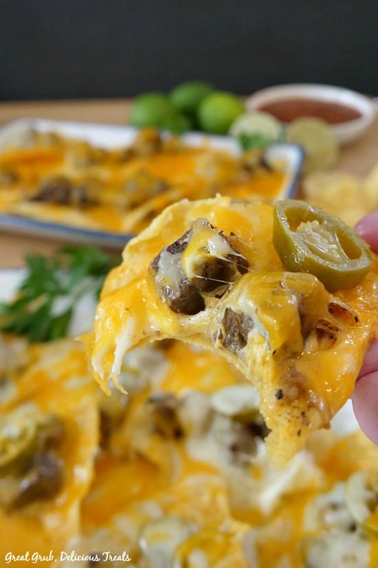 Rib Eye Nachos are loaded with meat, cheese and topped with jalapenos. Rib Eye Nachos - A picture of someone holding a tortilla chip with melted cheese, meat and a sliced jalapeno.