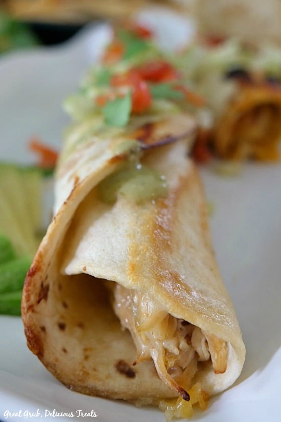 Spicy Chicken Flautas are baked until crispy and filled with a deliciously seasoned, slow cooked, chicken mixture and shredded cheese. Spicy Chicken Flautas - one single chicken flauta wrapped in a flour tortilla showing the chicken mixture peeking out of the end of the tortilla, garnished with a little shredded lettuce, diced tomatoes.