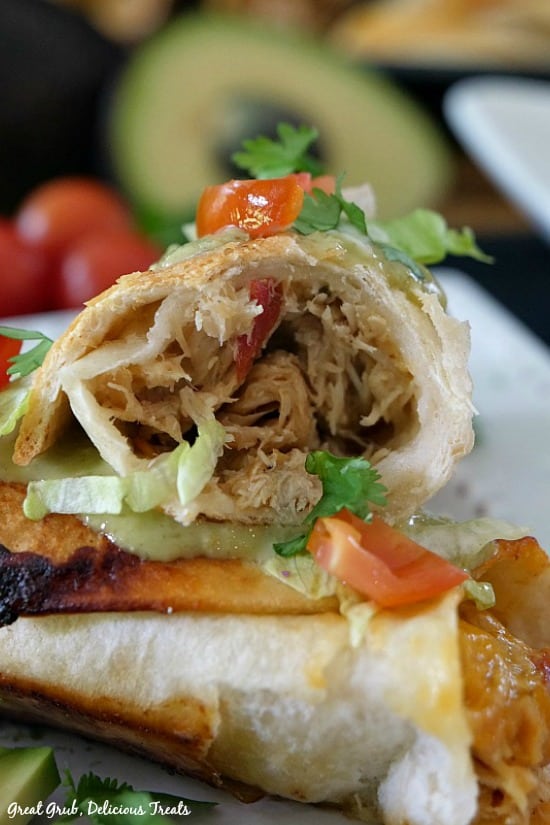 Spicy Chicken Flautas are a delicious Mexican food recipe using chicken breasts that has been slow cooked. Spicy Chicken Flautas - photo of a flauta and the inside chicken mixture leaning on the other flauta, both garnished with diced tomatoes and shredded lettuce.