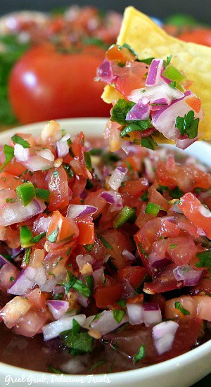 Pico de Gallo is a homemade chunky salsa dip recipe that is delicious served with tortilla chips or as a flavor enhancer for just about any Mexican dish. A close up of a tortilla chip that was dipped in the bowl of Pico de Gallo.