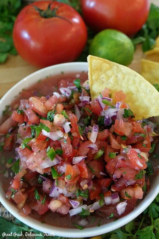 Pico de Gallo is so scrumptious, full of the freshest ingredients and is perfect to serve with tortilla chips. Pico de Gallo - a white bowl filled with chopped tomatoes, onions, cilantro, peppers with a chip placed in the bowl.