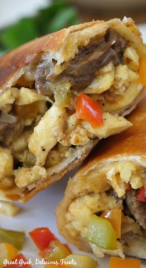 A super close up photo of a beef fajita breakfast burrito cut in half with the eggs, beef, pepper and onions showing stuffed into the tortilla.