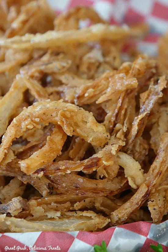 Fried Onion Strings are the perfect topping for burger, salads, and soups. A close up picture of fried onion strings on a red and white checked paper in a basket.