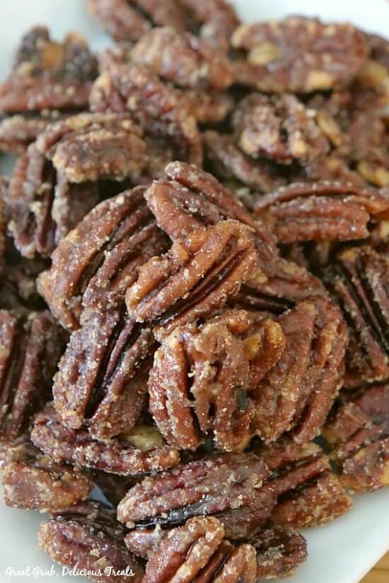 Homemade maple candied pecans is an incredibly delicious recipe that is perfect to take to parties or for a quick snack. Close up photo of maple candied pecans on a white plate.