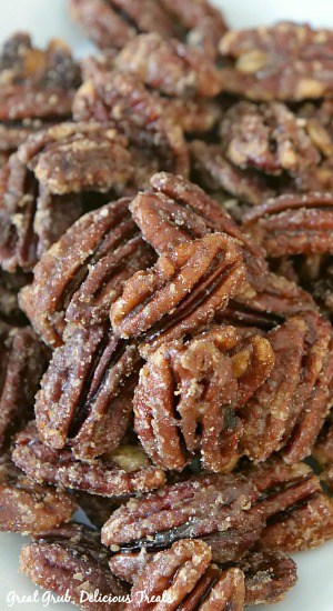 Homemade Maple Candied Pecans are a quick snack recipe that is great for the holiday season, loaded with maple and brown sugar flavor. Close up photo of maple candied pecans on a white plate.