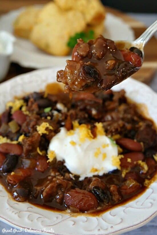 One pot kielbasa chili is a delicious recipe that makes a great weeknight dinner and is perfect for leftovers. A white bowl filled with chili, topped with sour cream and a white plate in the background with cornbread.