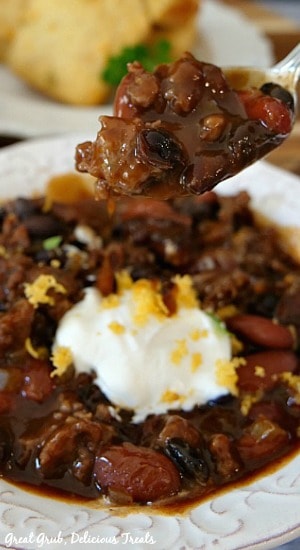 One Pot Kielbasa Chili is a great comfort food and the perfect chili recipe to make when it’s chilly outside. One Pot Kielbasa Chili - A white bowl of chili with a spoonful of hearty chili, with a white plate with cornbread in the background.