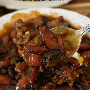 A close up picture of a spoonful of chili in a white bowl.