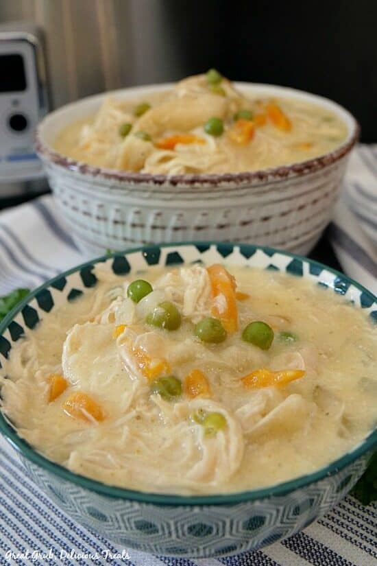 Crockpot Chicken and Dumplings is a delicious and perfect crockpot recipe to save for cold days. a teal and white spotted bowl with chicken and dumplings with a white and burgundy bowl in the background.