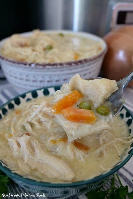Crockpot Chicken and Dumplings in a delicious crockpot recipe and the perfect comfort food to make on a chilly night. A teal and white spotted bowl with a bite of chicken and dumplings on a fork.