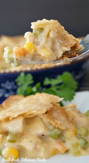 Easy Chicken Pot Pie is a delicious chicken recipe that is full of veggies, seasoned chicken, and a creamy base. A piece of chicken pot pie on a fork with a slice of pot pie on a white plate garnished with parsley with a blue pie pan in the background