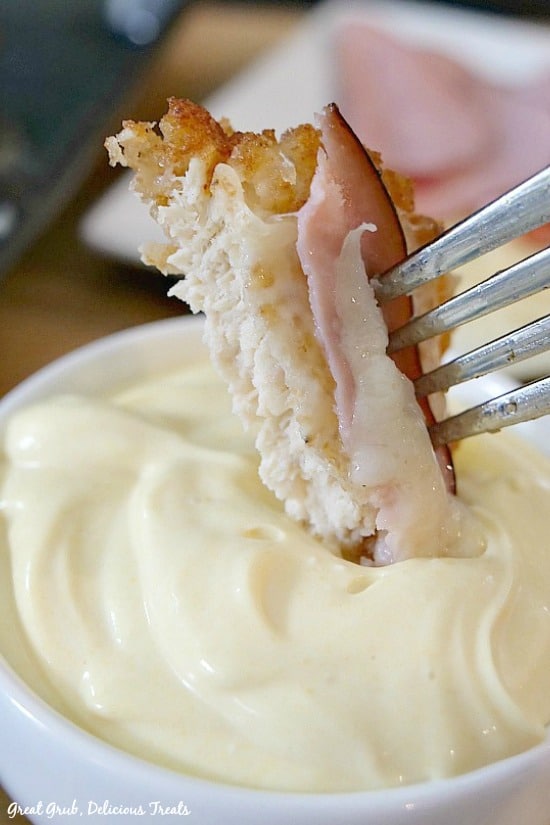 Malibu Chicken is a delicious and favorite copycat Sizzler recipe that is breaded, fried and topped with Swiss cheese and ham, then baked until the cheese is melted. A bite size piece of Malibu Chicken on a fork being dipped into a mayonnaise/mustard dipping sauce.