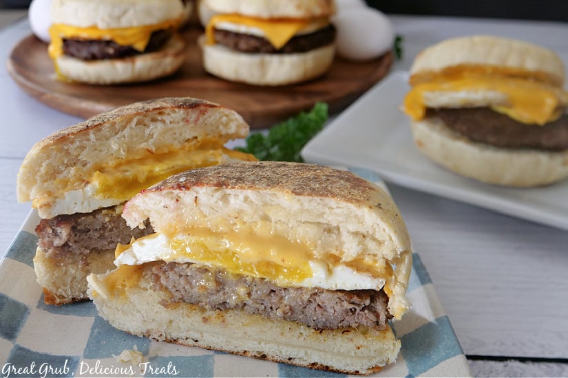 Sausage and Egg Breakfast Sandwiches are an amazing recipe for breakfast and are great to freeze for later. A sandwich sitting on a blue and white checkered plate and cut in half where you can see the sausage, egg, and cheese.
