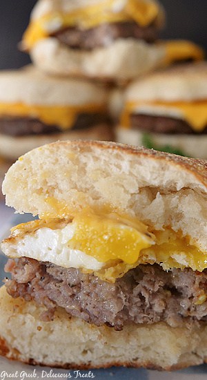 Homemade Breakfast Sandwiches are a delicious breakfast recipe that are made with sausage patties, eggs, a homemade English muffin, and a slice of cheese. A close up photo of a breakfast sandwich with a bite taken out of it where you can see the sausage, egg, and cheese in between the English muffin.