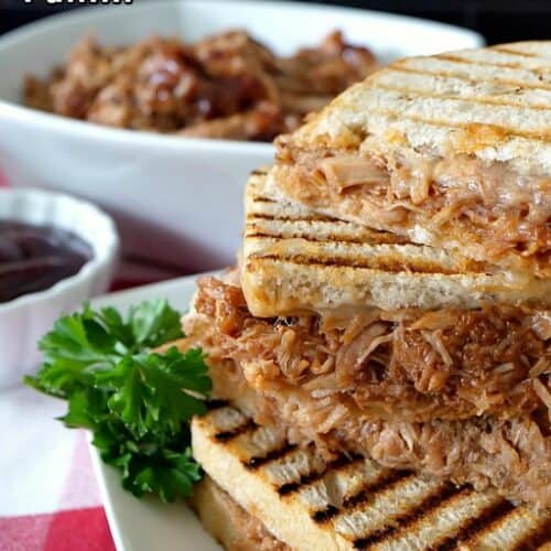 BBQ panini sandwich on a white plate with a white bowl of pulled pork in the background.