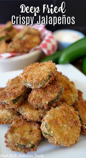 Deep Fried Crispy Jalapenos are deep fried, crunchy and seasoned perfectly and a favorite appetizer recipe. Deep fried jalapenos on a white plate with a white bowl, jalapenos, and ranch dressing in the background and.