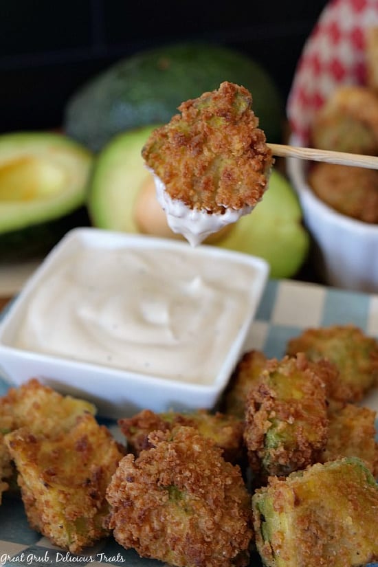 Crispy Fried Avocado Bites are bite sized pieces of avocados coated with a delicious bread crumb mixture and fried until crispy. Crispy Fried Avocado Bites on a light blue and white checkered plate with one bite being dipped in ranch dressing.