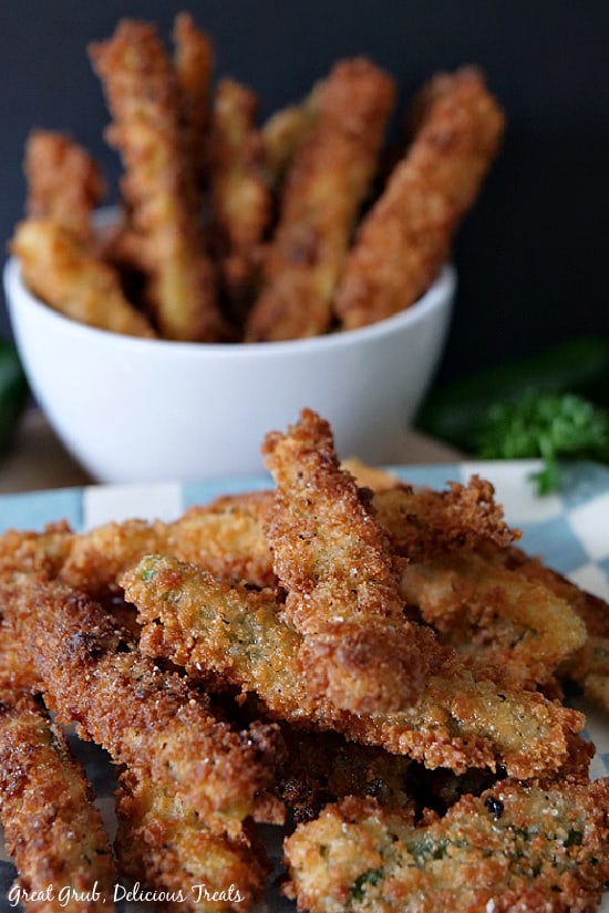Crispy Jalapeño Fries are a delicious snack and appetizer recipe that are so delicious with a crispy, crunchy coating. A light blue and white checkered plate with crispy jalapeno fries and a small white bowl with more jalapeno fries in it.