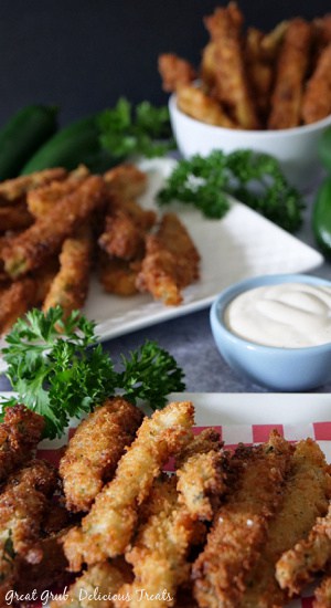 Crispy Jalapeño Fries are seasoned perfectly, fried to perfection and make a delicious appetizer recipe the whole family will enjoy. Jalapeno fries on a stacked up on a red and white checkered liner on top of a white plate, a small light blue bowl with ranch dressing, a white plate and a small white bowl in the background all with fried jalapenos on them.
