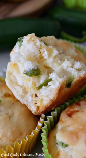Jalapeño Cheese Muffins are a delicious jalapeno muffin recipe that is loaded with sharp cheddar cheese and just the right amount of spice. A close up of a split Jalapeno Muffin with butter melting on one half, sitting on top of more jalapeno muffins with jalapenos in the background.