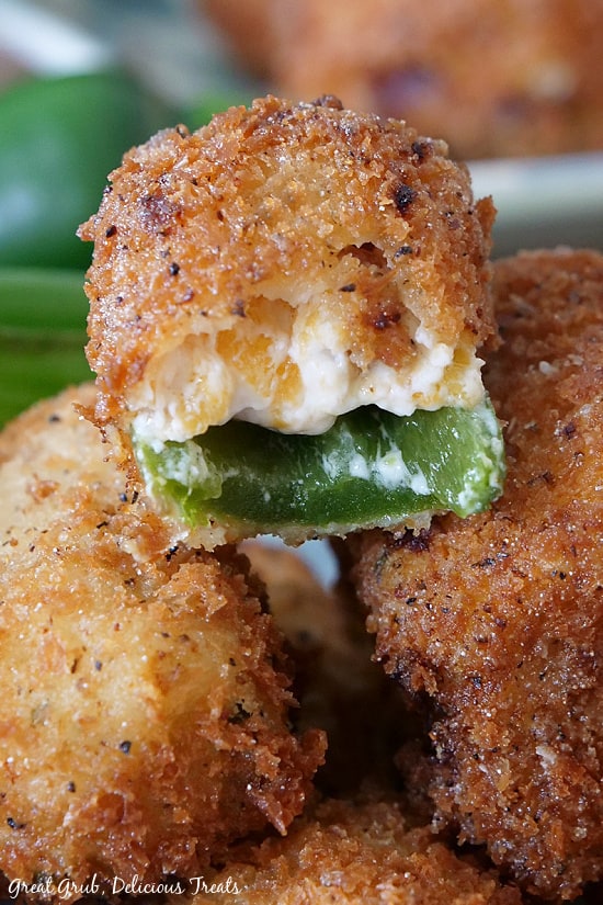 Stuffed Jalapeno Poppers are a deliciously crispy appetizer recipe seasoned perfectly, loaded with cream cheese, bacon, green onions and cheese, then deep fried. An extreme close up of a Stuffed Jalapeno Popper with a bite taken, sitting on top of two others, showing the jalapeno and cream cheese mixture.