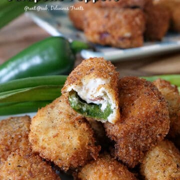 Stuffed jalapeno poppers stacked up on a white plate with a bite taken out of one of them, with green onions and a jalapeno in the background, and another white plate with jalapeno poppers stacked up.
