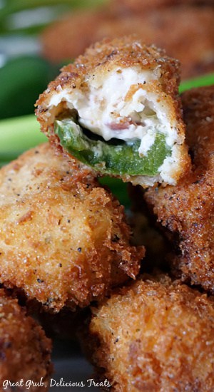 Stuffed Jalapeño Poppers make the perfect appetizer recipe full of crispy bacon, cream cheese, shredded cheese and green onions. Stuffed jalapeno poppers stacked up and a bite taken out of a popper where you can see the jalapeno and the cheesy filling.