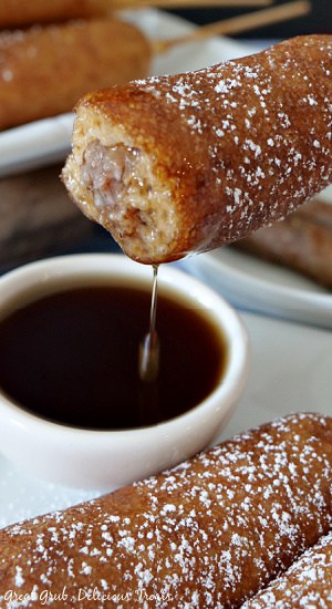 Pancake Sausage on a Stick is a great breakfast recipe that the whole family will enjoy. A pancake sausage on a stick with a bite taken out out and dipped in maple syrup.