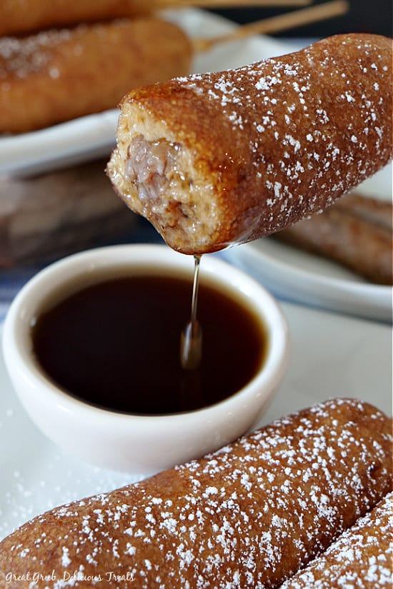 Pancake Sausage on a Stick is a delicious breakfast idea that is not only convenient but a pancake recipe everyone will enjoy. A Pancake Sausage on a Stick after a bite has been taken and after it has been dipped in syrup, showing the syrup dripping off the pancake on a stick.