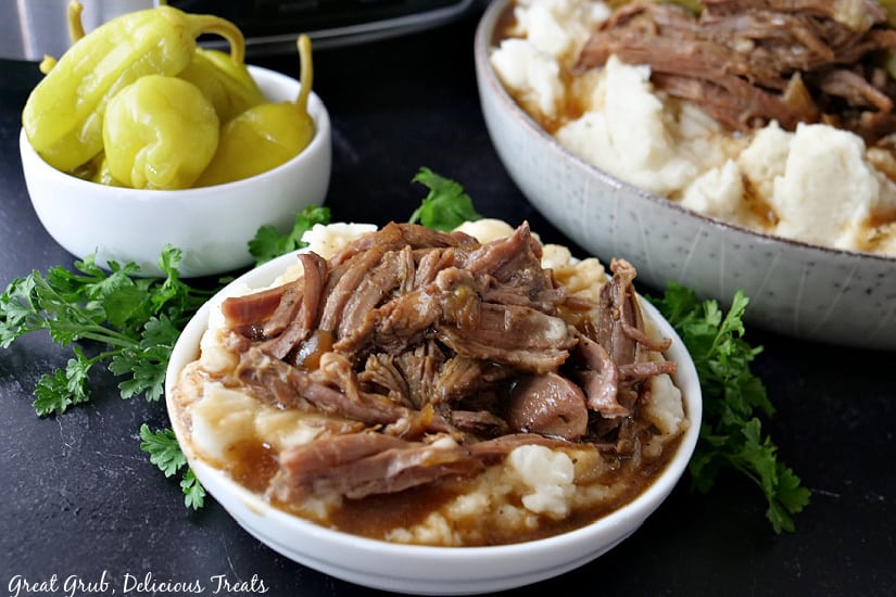 A black surface with 3 bowls, two with mashed potatoes and pot roast in them and another with pepperoncinis in it.