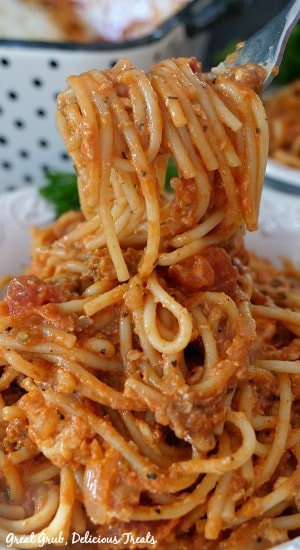 Italian Sausage Spaghetti Bake is one delicious pasta recipe loaded with Italian sausage, cream cheese, mozzarella cheese and more. A forkful of Italian Sausage Spaghetti Bake being held up over a white bowl filled with the spaghetti bake.