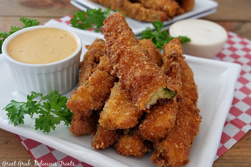 A white plate with a stack of fried zucchini on it with a white bowl of dipping sauce.